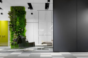 Lindner Life Glastrennwand - dahinter begrünte Wand, Sessel und Couch.